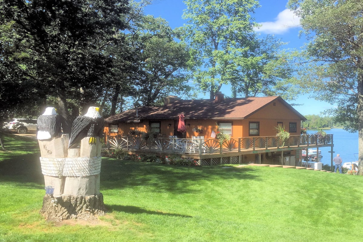 A house with a deck overlooking a lake, surrounded by trees.