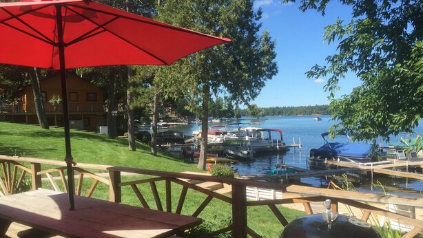 Una terraza de madera con una mesa de picnic y una parrilla barbacoa, con vistas a un lago con barcos.