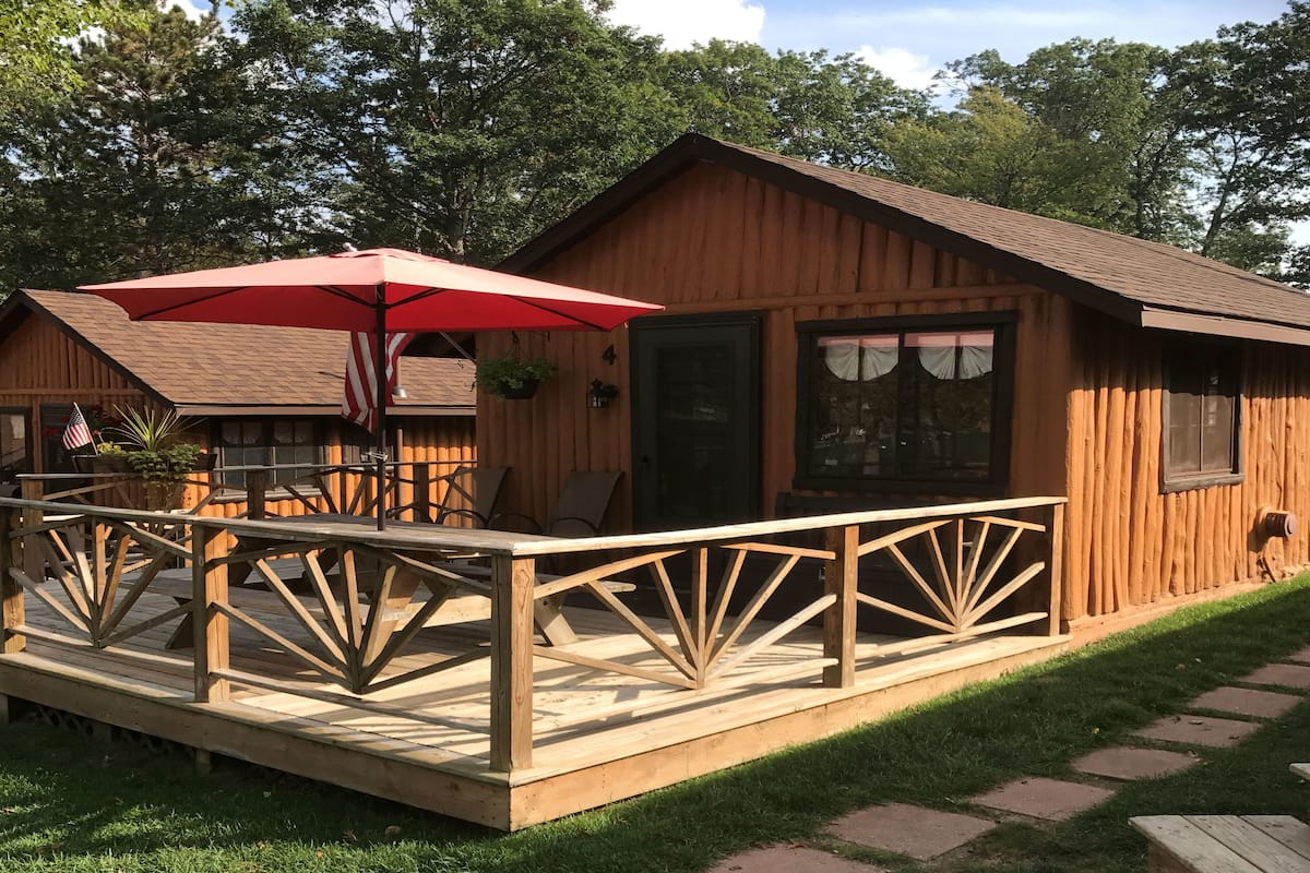 A wooden cabin with a deck, a red umbrella, and an American flag.