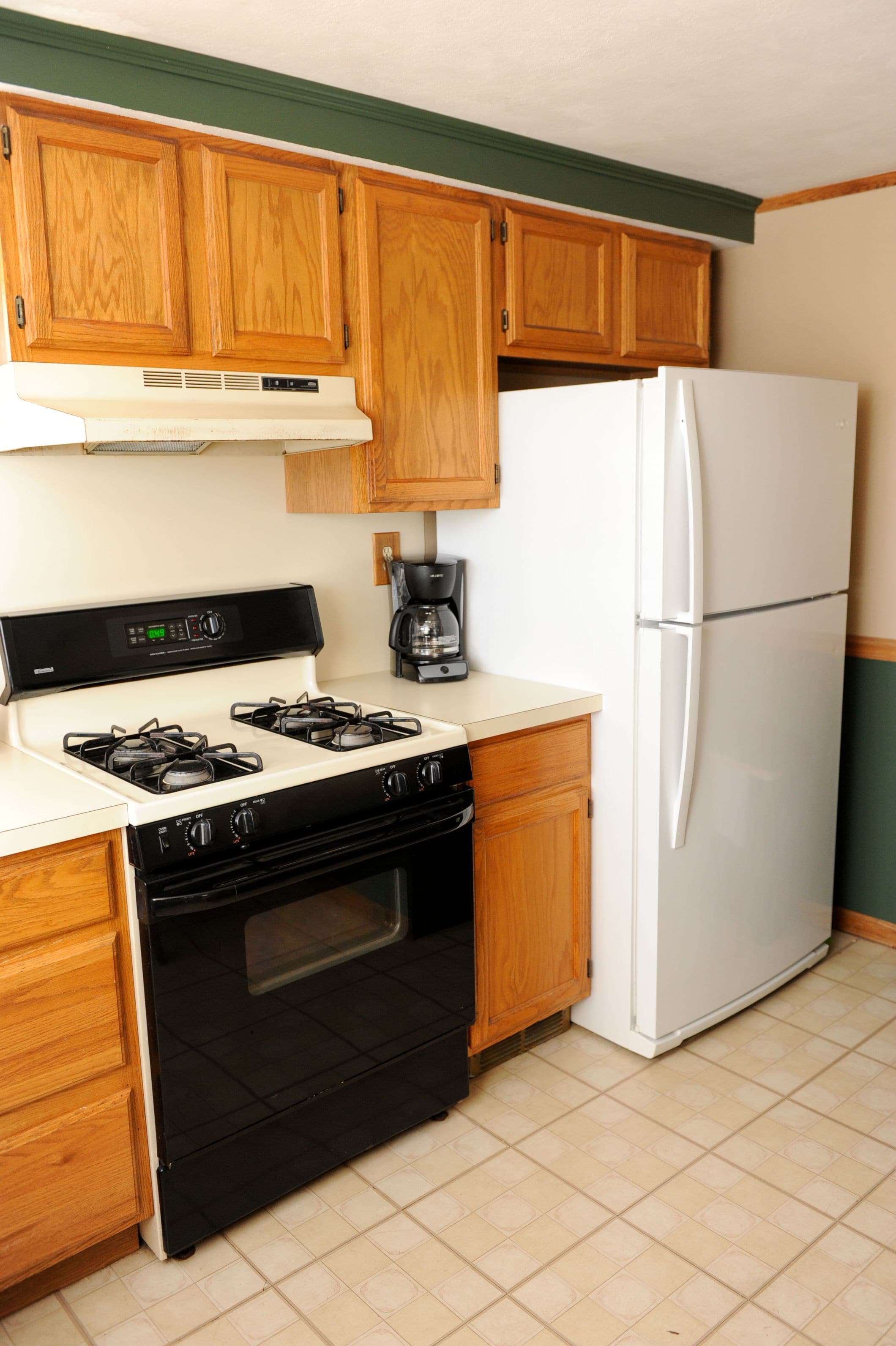 A kitchen with wooden cabinets, a white stove, a black oven, and a white refrigerator.