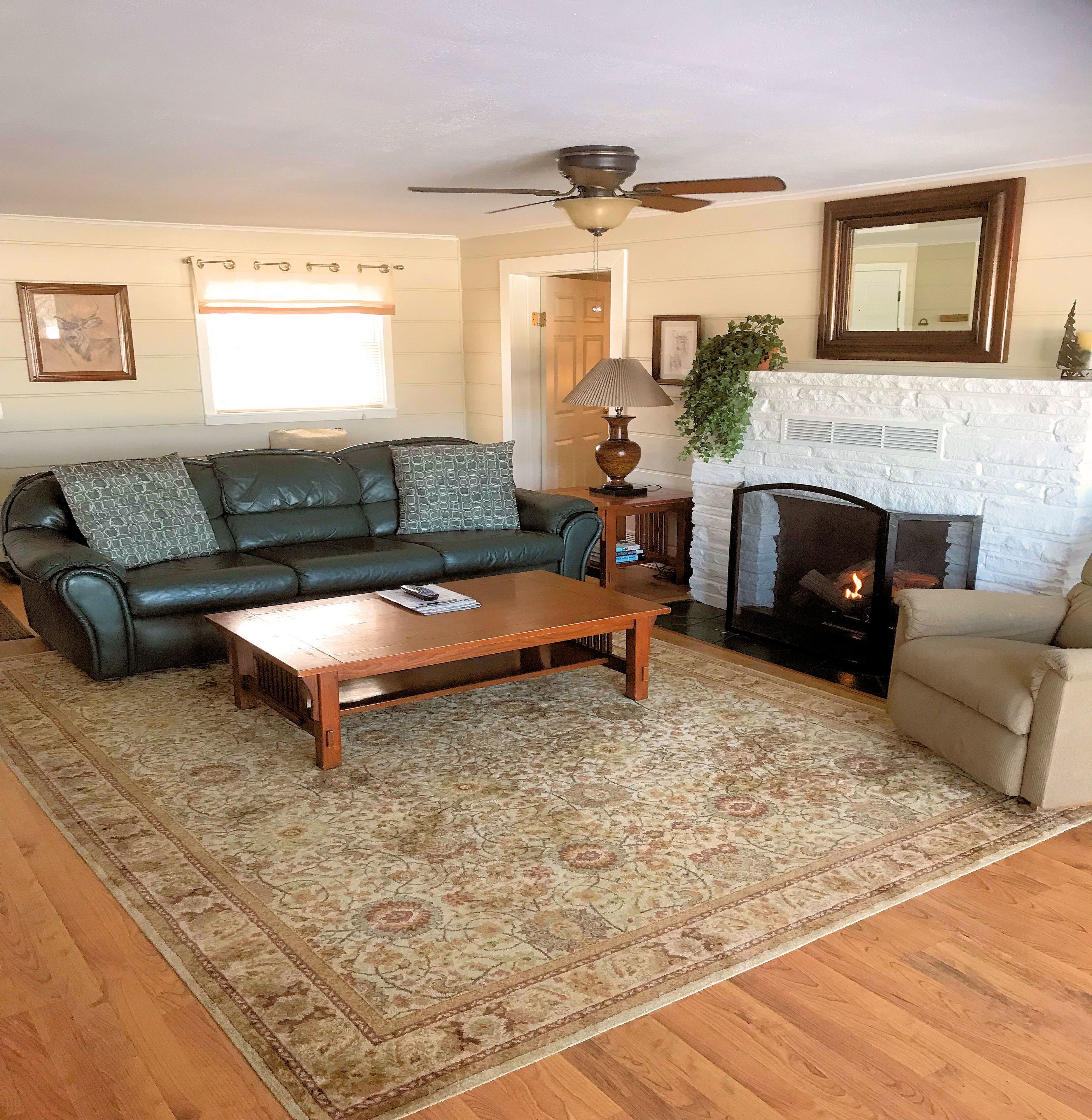 A living room with a sofa, a coffee table, a fireplace, and a ceiling fan.