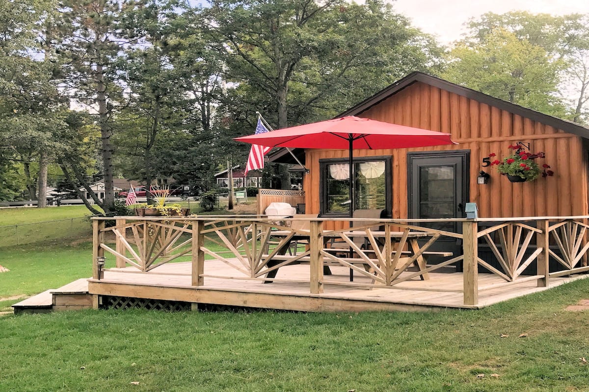 A wooden cabin with a deck, a red umbrella, and an American flag.