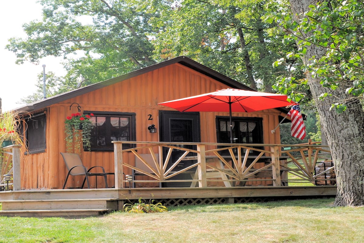 A wooden cabin with a porch, a number '2' sign, and a red umbrella.