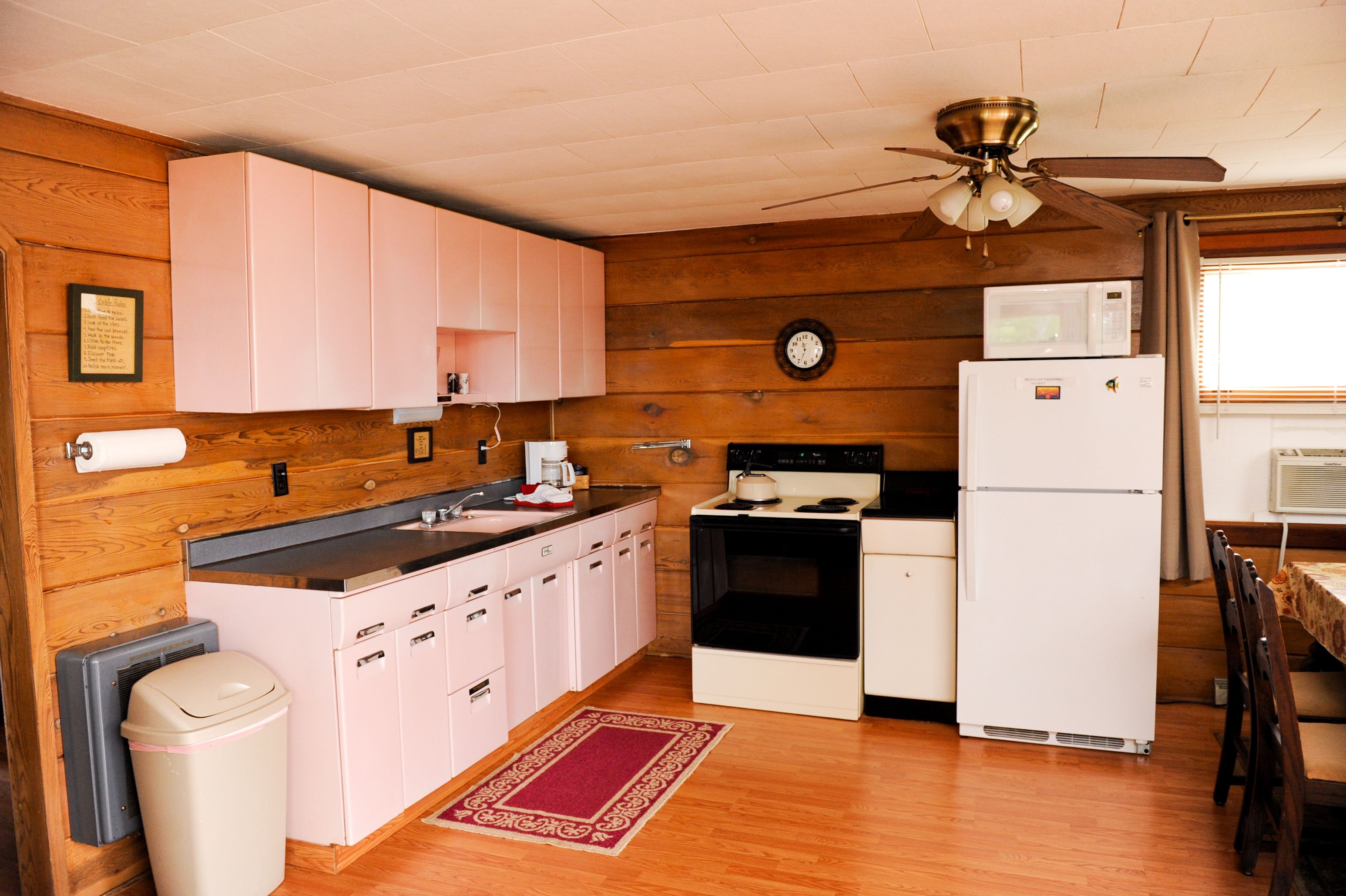 Una cocina compacta con paredes de madera, un ventilador de techo, un microondas, un refrigerador y un lavamanos.