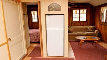 Una habitación acogedora con una cama, un sofá, una mesa de madera y un refrigerador.