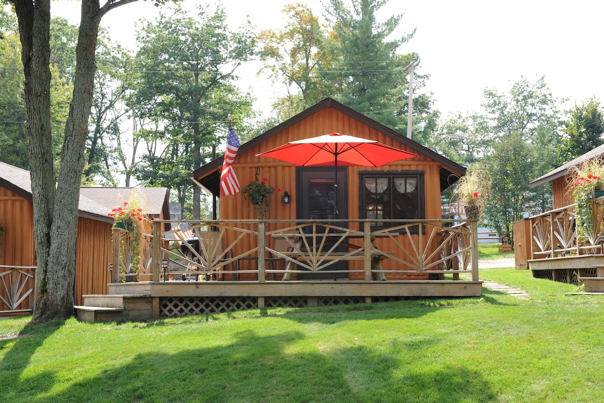 A wooden cabin with a porch, a red umbrella, and an American flag.