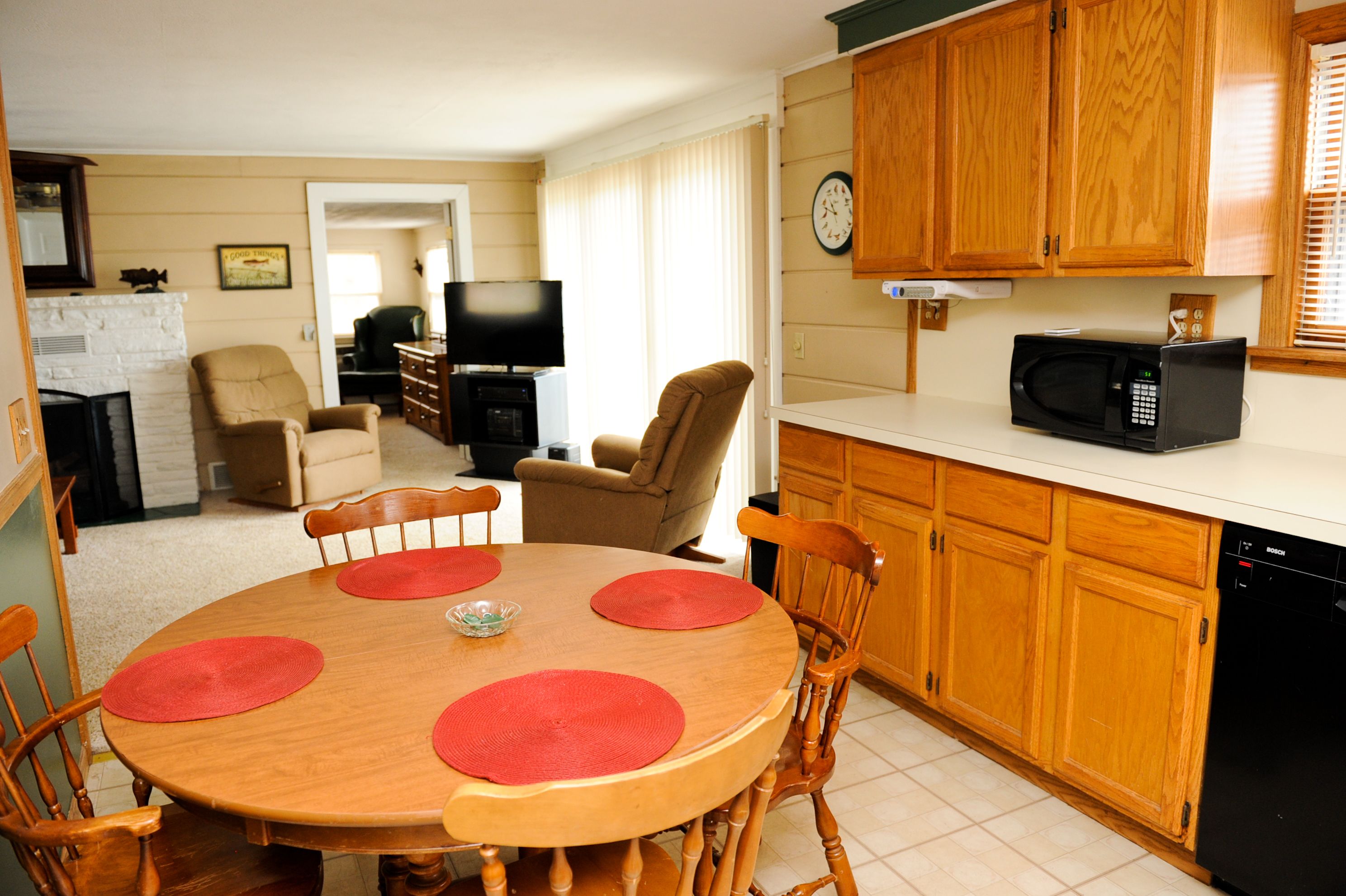 Un coin repas avec une table et des chaises en bois, un téléviseur en arrière-plan et des meubles de rangement en bois dans la cuisine.