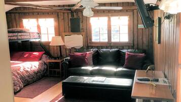 Una habitación acogedora estilo cabaña con cama, sofá, una mesita y ventilador de techo.