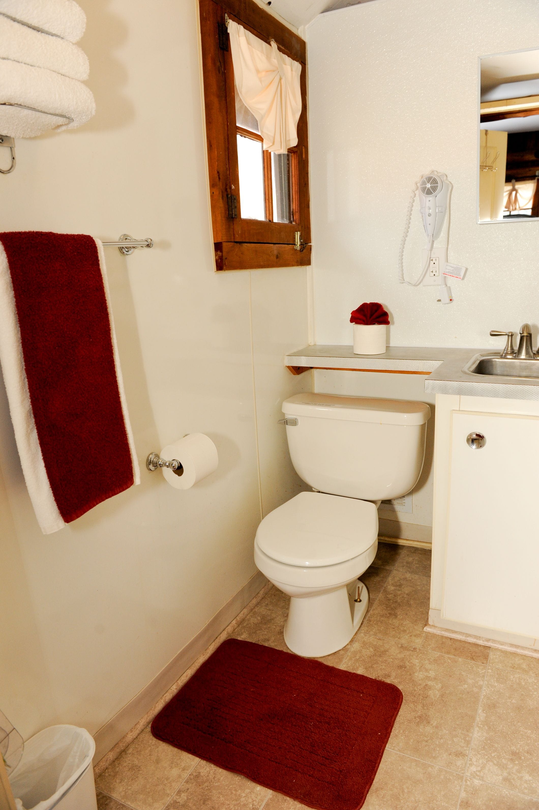 A bathroom with a toilet, a sink, a mirror, and a red bath mat.