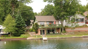 Una cabaña junto al lago con un muelle, una terraza y un pequeño jardín.