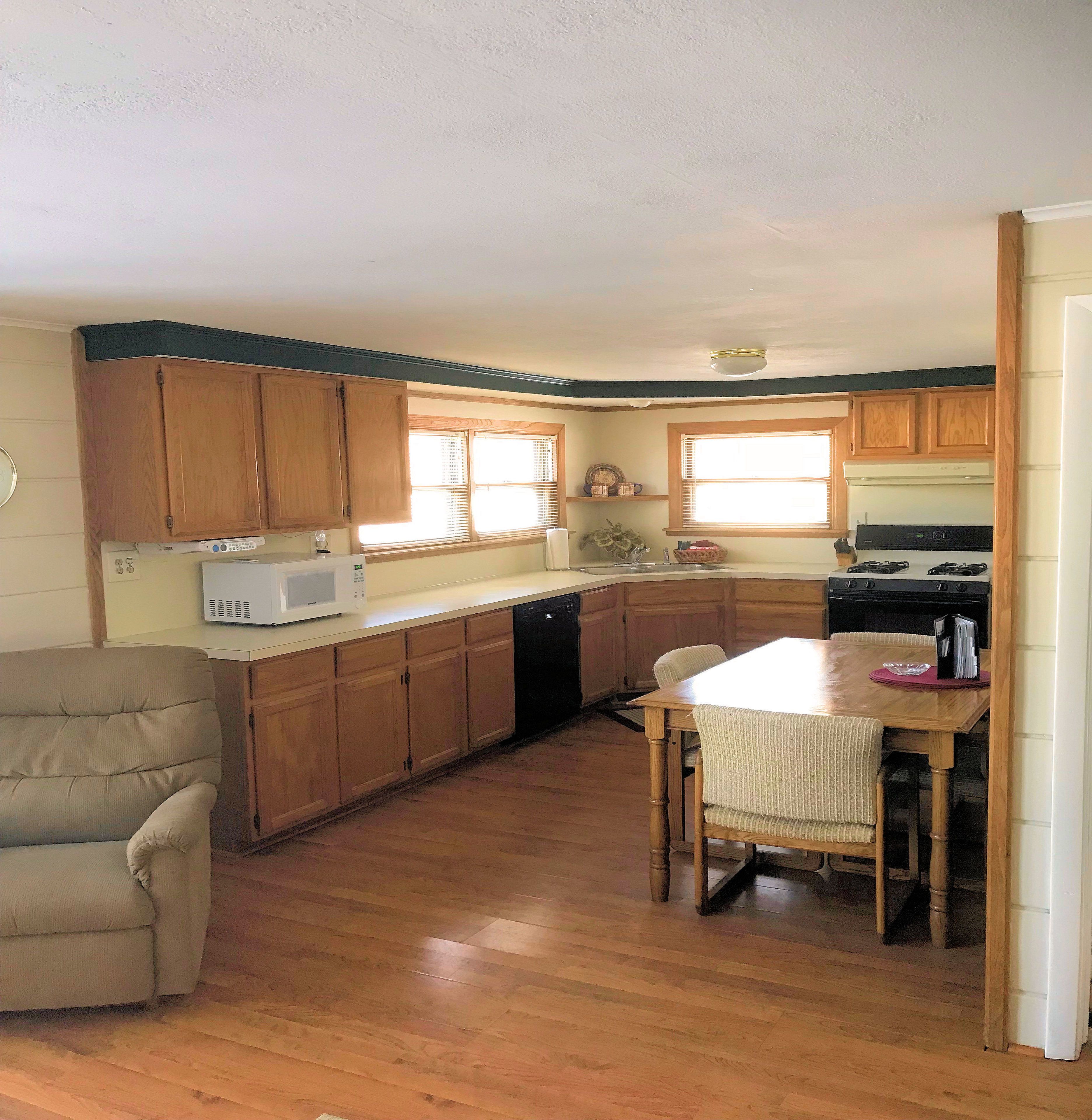 Una cocina compacta con armarios de madera, microondas, lavavajillas y una zona de comedor con mesa y sillas.