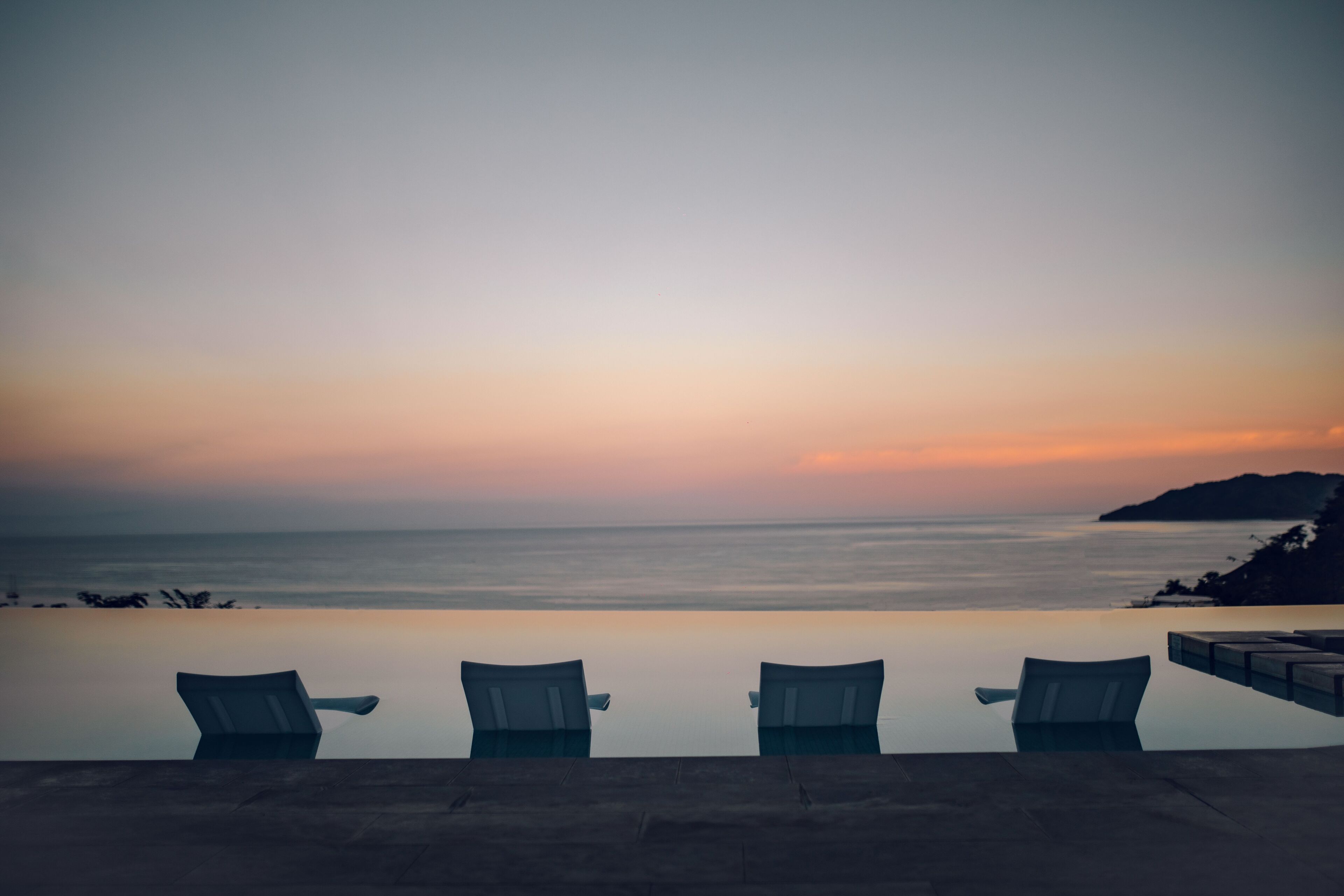 Una piscina a sfioro con tre lettini che si affacciano su un tramonto sull'oceano.