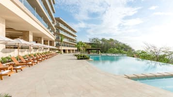 Ein Hotelpoolbereich mit Liegestühlen und Sonnenschirmen, einem wolkenlosen Himmel und einem großen Pool.