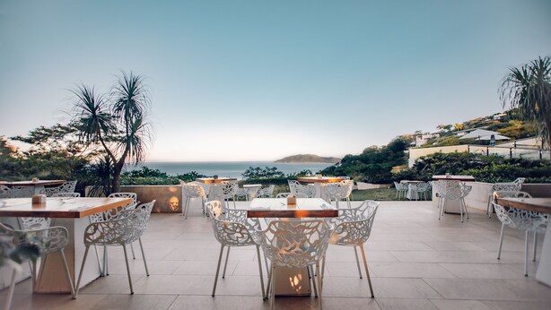 An outdoor patio with white chairs and tables, overlooking a scenic view of the ocean and hills. - Wyndham Tamarindo (Tamarindo)