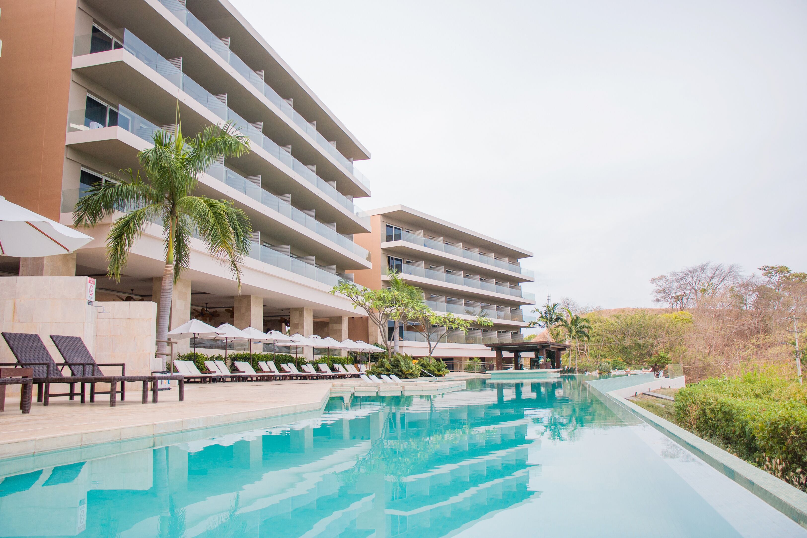 A hotel with a swimming pool, multiple balconies, and lounge chairs.