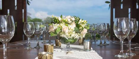 Una mesa dispuesta con copas de vino y un centro de flores, con vistas al cielo y follaje en el fondo.