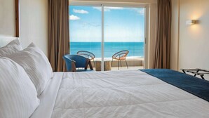 Habitación de hotel con una cama grande, dos sillas y vista al océano, además de una puerta corrediza de vidrio.