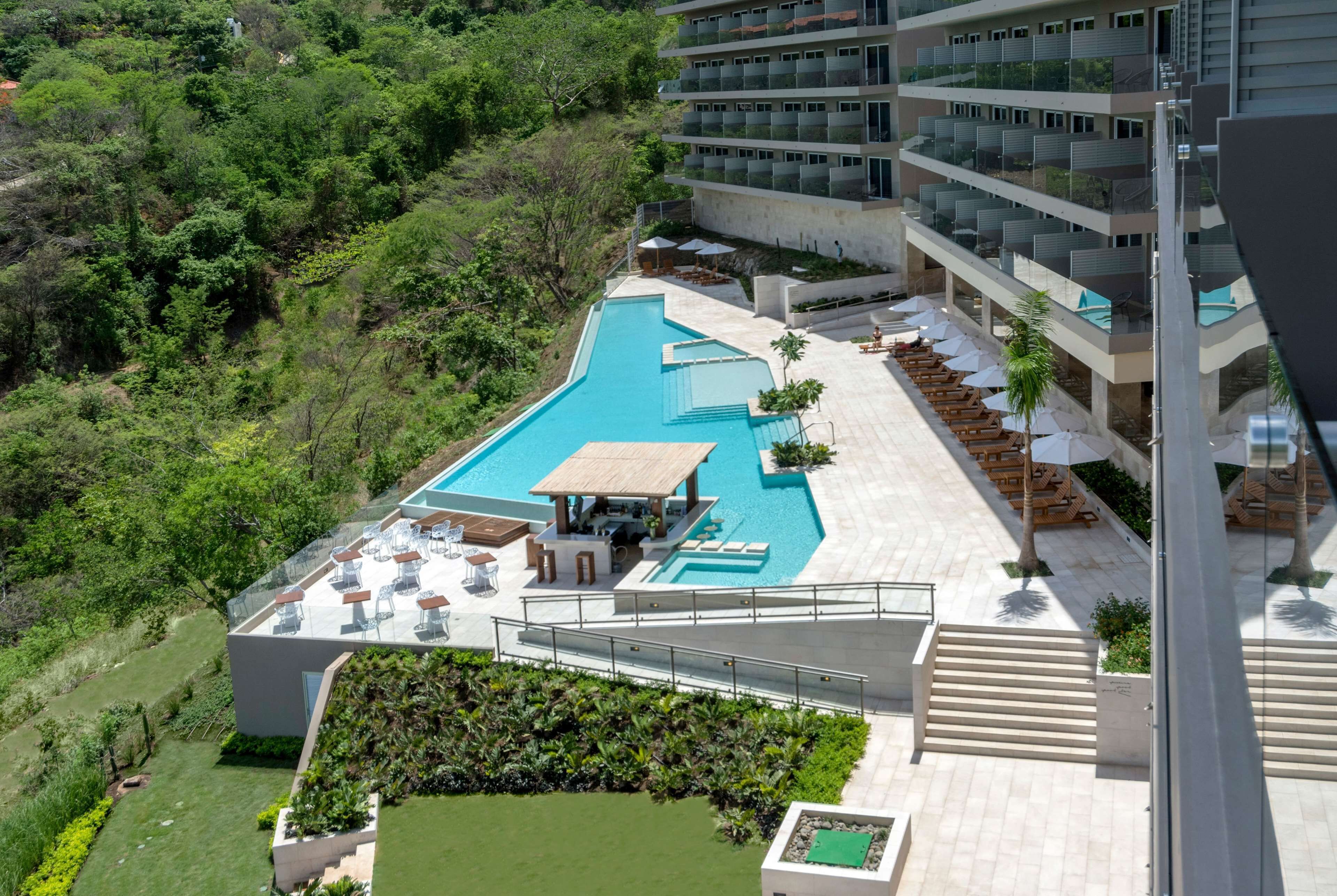 Un hôtel moderne doté d’une piscine, d’un espace extérieur aménagé et d’une végétation luxuriante.