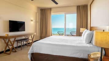 Una habitación de hotel con una cama, un escritorio, televisión, teléfono y vista al océano.