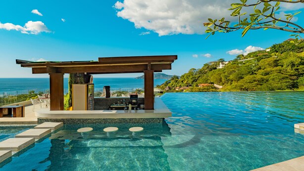 Zona junto a la piscina con un pérgola, asientos y vistas al océano.