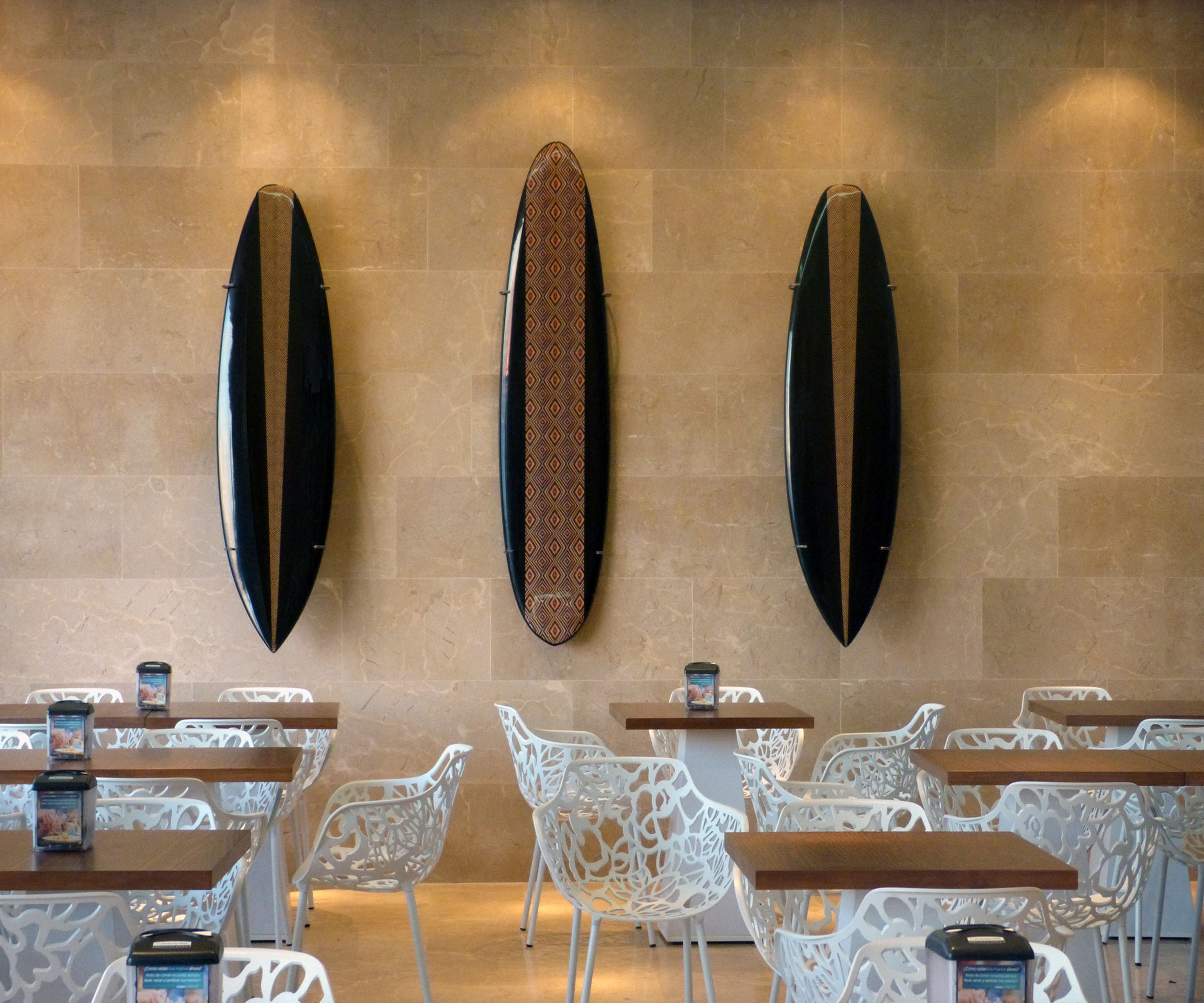 A restaurant interior with white chairs, tables, and surfboard-shaped wall decor.
