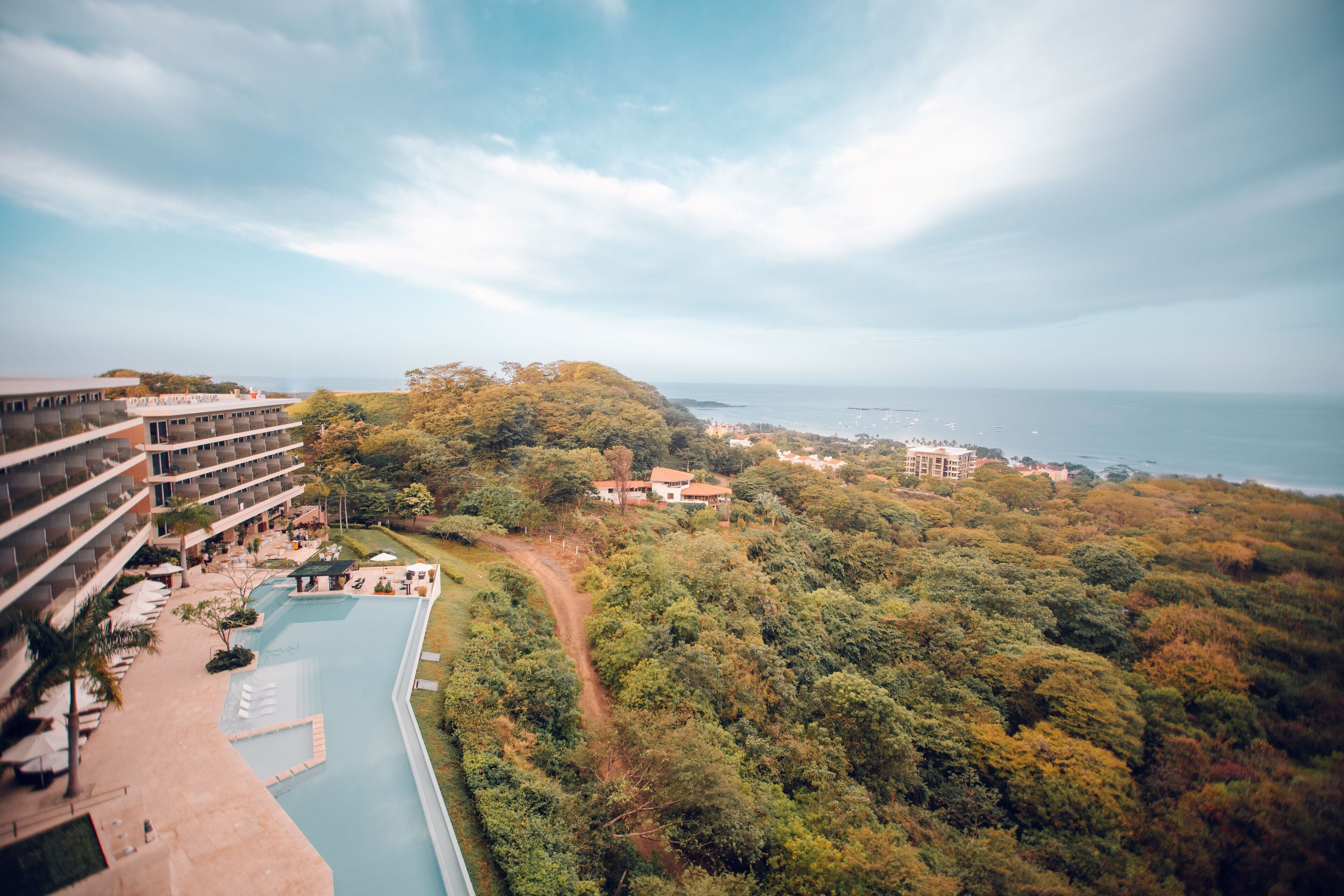 A resort with a pool, lush greenery, and a view of the ocean.
