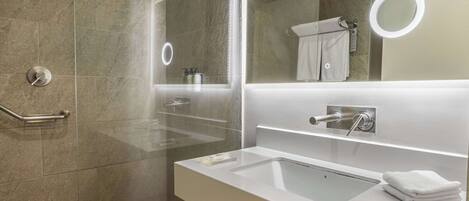 A modern bathroom with a glass shower enclosure, a white sink, and a mirror with a built-in light.