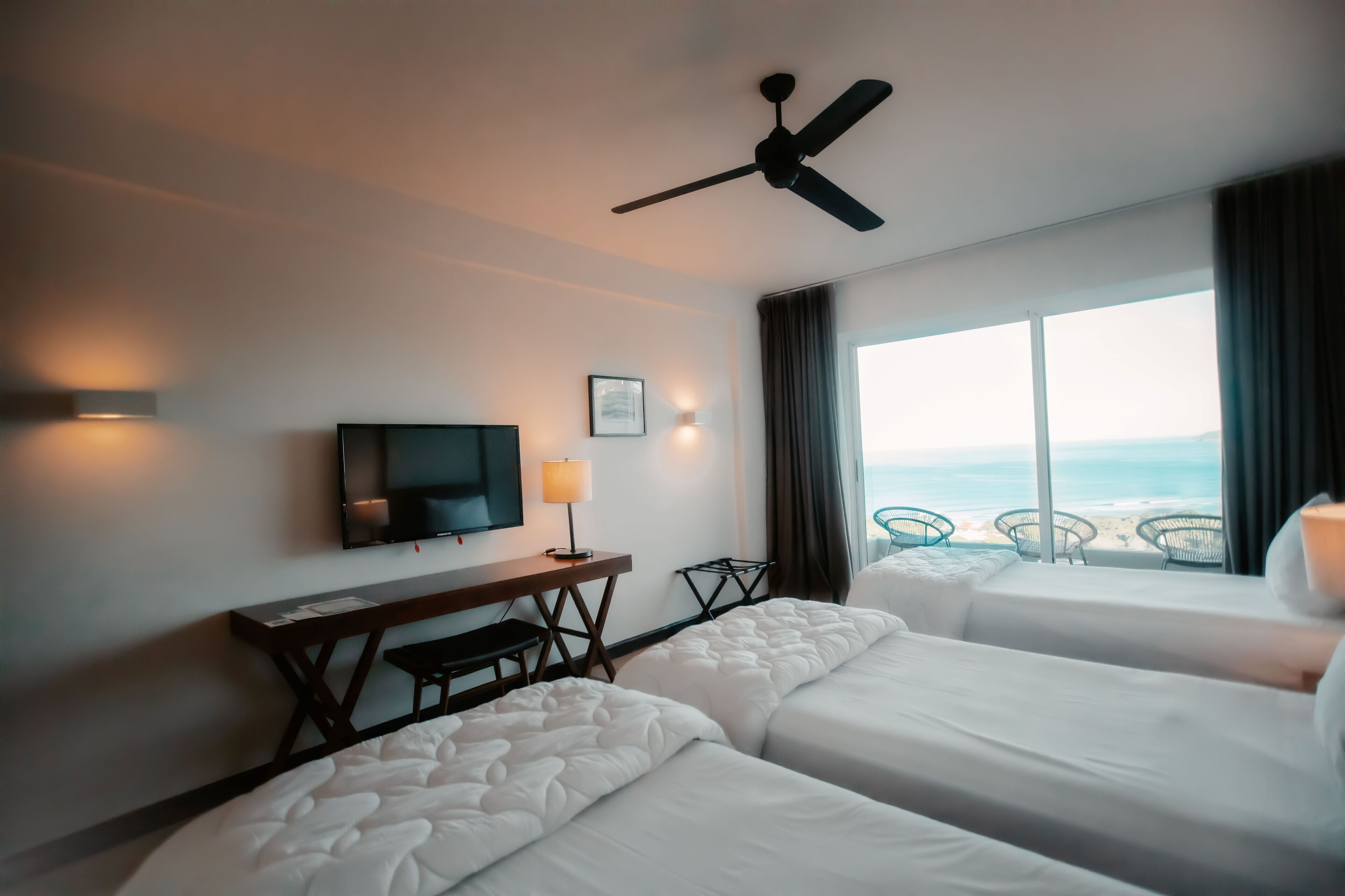 Habitación de hotel con dos camas, un escritorio, televisión y vista al océano.