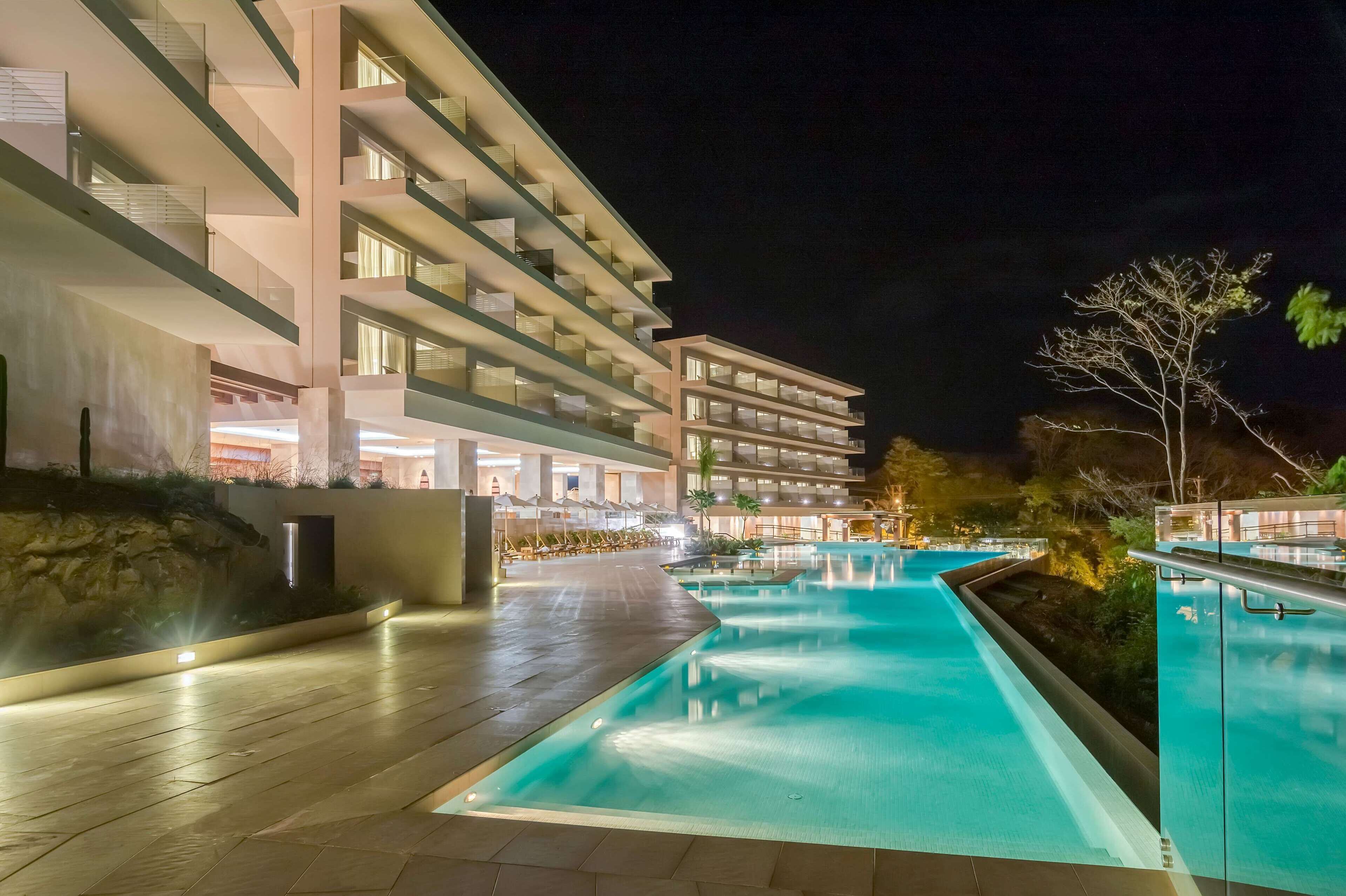 A modern hotel with a swimming pool, multiple balconies, and a well-lit outdoor area.