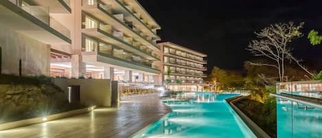 A modern hotel with a swimming pool, multiple balconies, and a well-lit outdoor area.