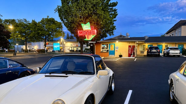 Ein Parkplatz mit einem weißen Cabrio, einem Motel-Schild und einem Gebäude mit einer blauen Tür.