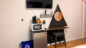 Eine kompakte Küchenzeile mit Mikrowelle, Kaffeemaschine und kleinem Kühlschrank. Ein Fernseher ist über der Küchenzeile an der Wand befestigt.