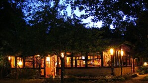 Edifici rústic amb diverses finestres i façana de fusta, envoltat d'arbres i il·luminat per llums càlides.