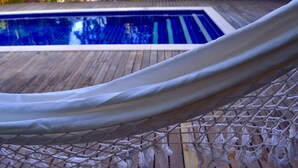 Una cadira d'hamaca sobre un pont de fusta, amb una piscina al fons.