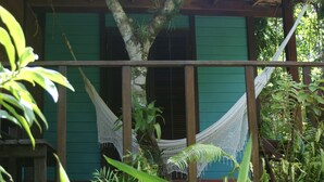 A hammock between wooden beams, a green building with shutters, and lush tropical foliage. - Pousada Quinta do Caju (Cairu)