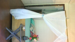A room with a bed covered by a white canopy, a wooden floor, a teal sofa with floral cushions, and a small table with a vase of flowers. - Pousada Quinta do Caju (Cairu)