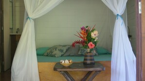 A room with a bed, a small table with a vase of flowers, and a bowl of snacks. - Pousada Quinta do Caju (Cairu)