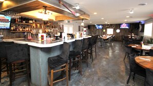 A bar area with a counter, stools, and a variety of bottles and glasses. There are tables and chairs in the dining area, and a television is mounted on the wall. - Sweetgrass Inn B&B (Rapid City)