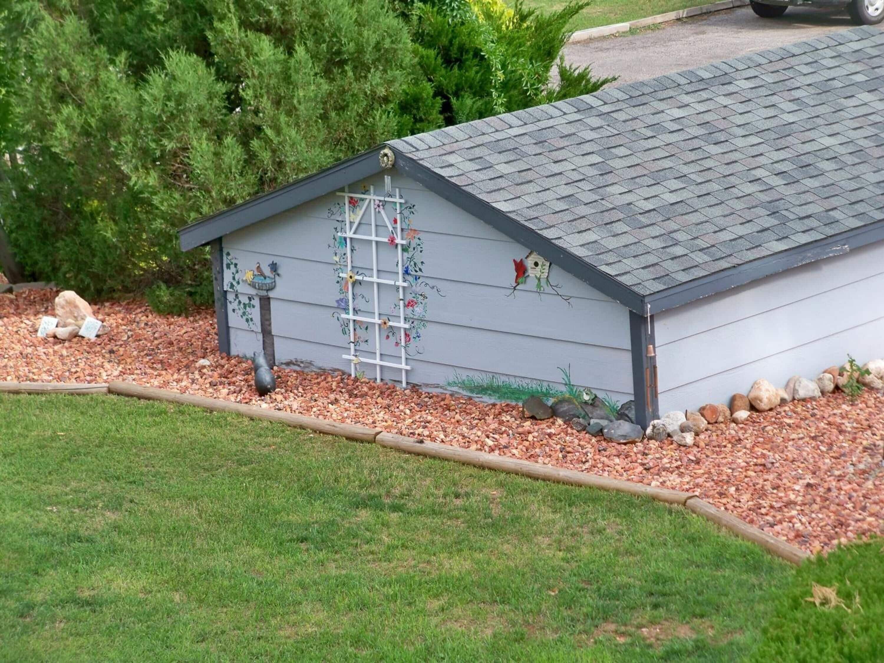 A small, single-story building with a sloped roof, a ladder, and decorative elements like a birdhouse and flowers on the exterior wall.