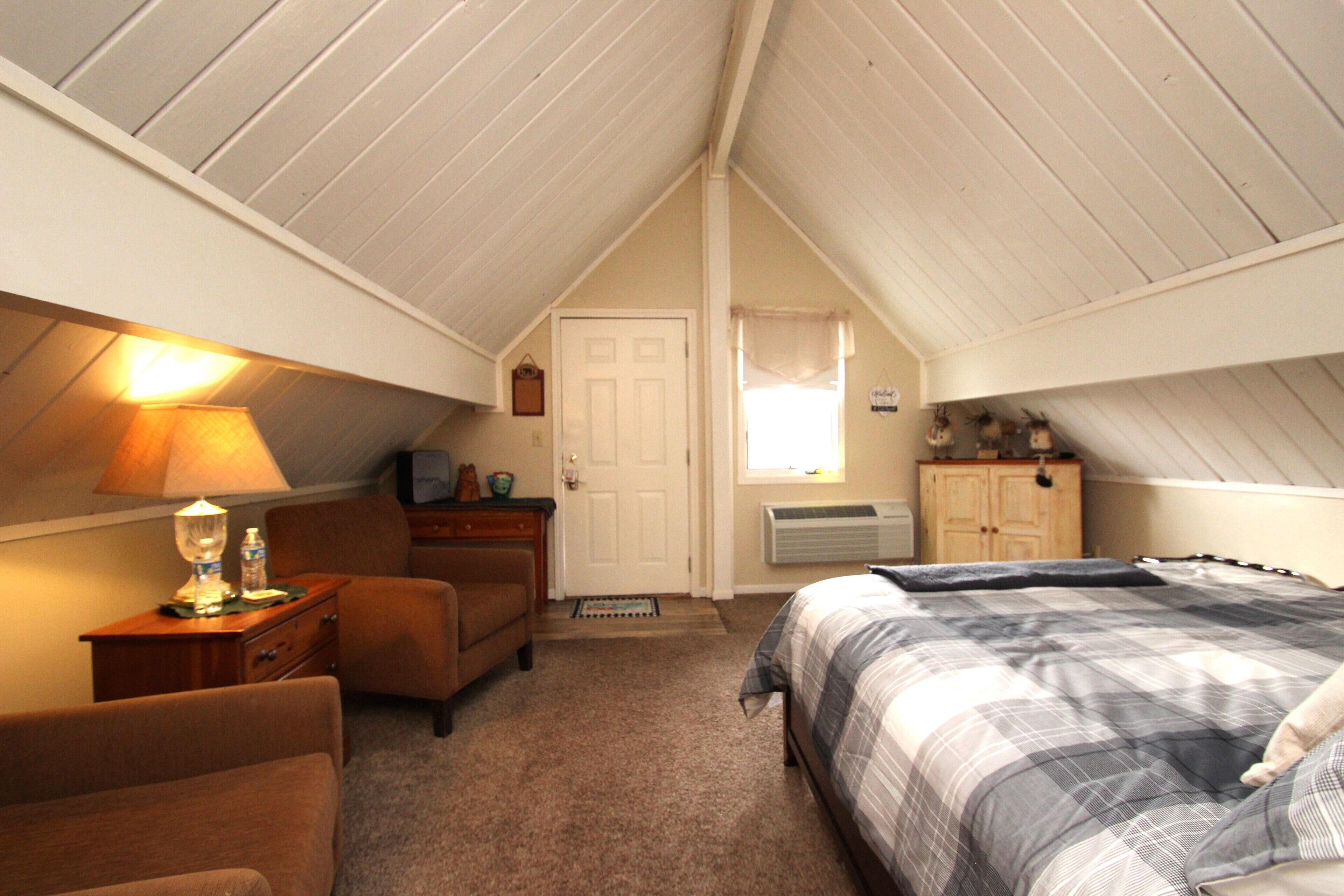 A bedroom with a bed, a nightstand, a lamp, a dresser, and a window.