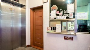 Un ascensor, una puerta de madera y un mostrador de recepción con letreros y avisos.