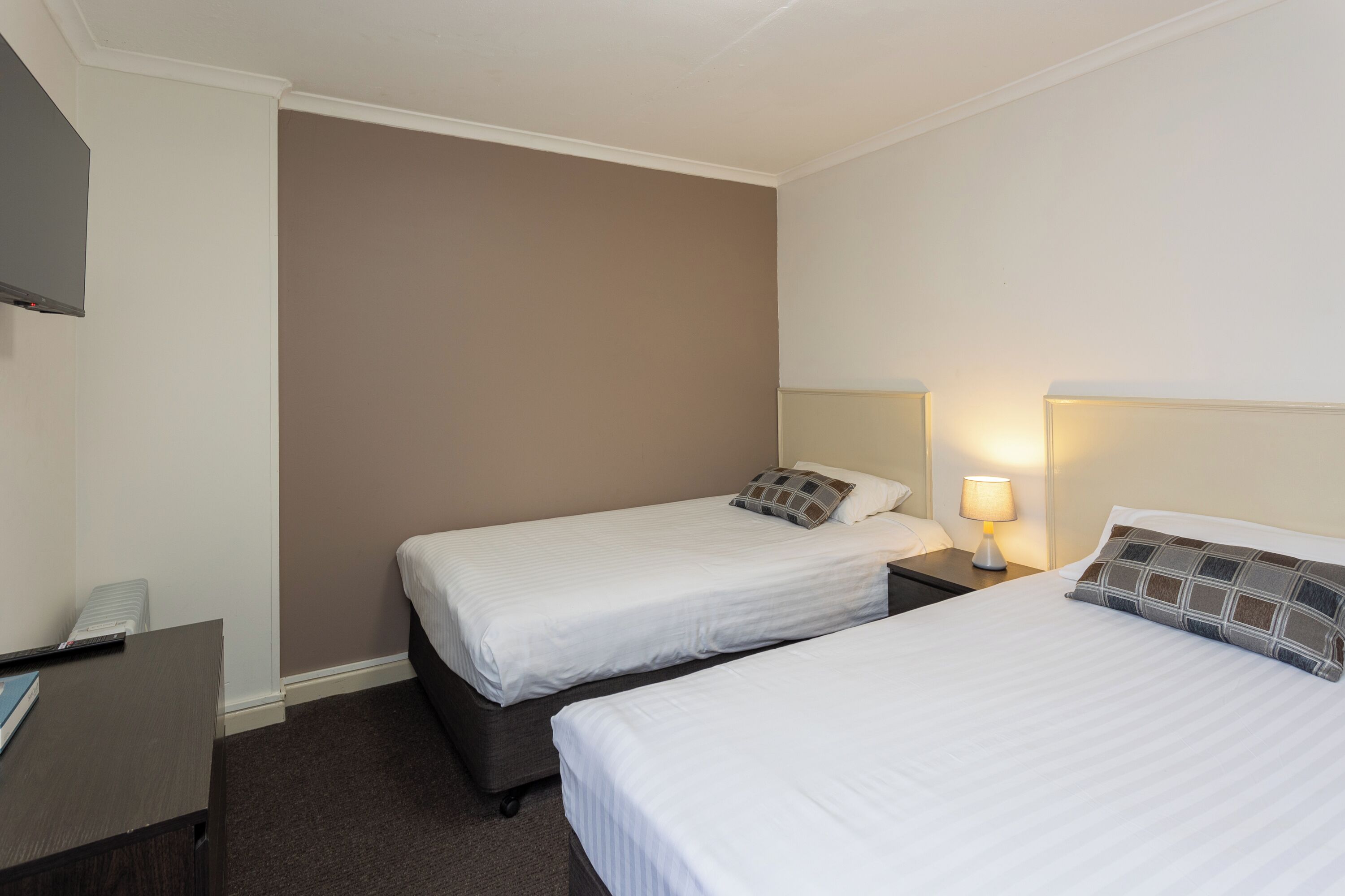 A hotel room with two single beds, a desk, and a TV mounted on the wall.