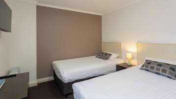 Habitación de hotel con dos camas individuales, un escritorio y un televisor montado en la pared.