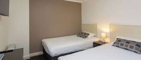 A hotel room with two single beds, a desk, and a TV mounted on the wall.