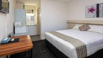 Una habitación de hotel con cama, escritorio, silla, kitchenette pequeña y baño.