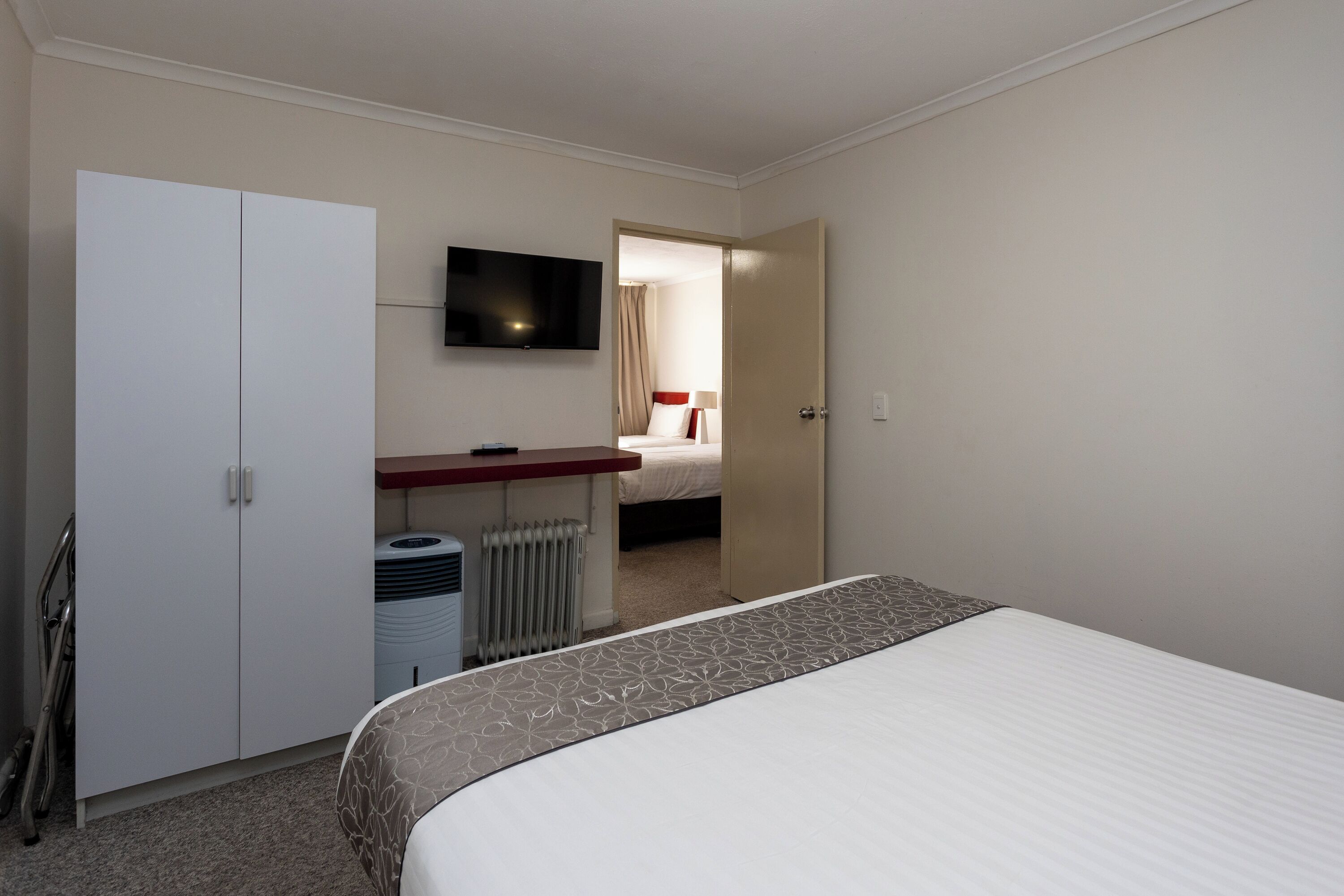 Une chambre d’hôtel comprenant un lit, un bureau avec une télévision, une armoire et un radiateur.