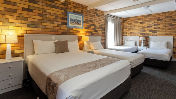 A hotel room with two beds, a brick-patterned wall, and a framed picture. - Fig Tree Motel (Narrandera)