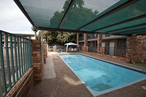 A rectangular swimming pool with a tiled edge, surrounded by a brick wall and a green metal fence.