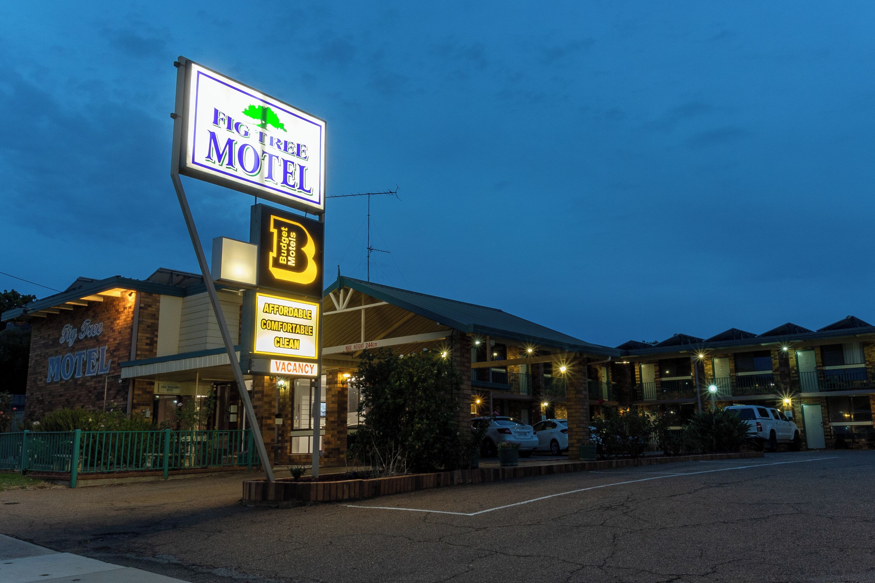 A motel with a large sign, a covered parking area, and multiple buildings in the background.