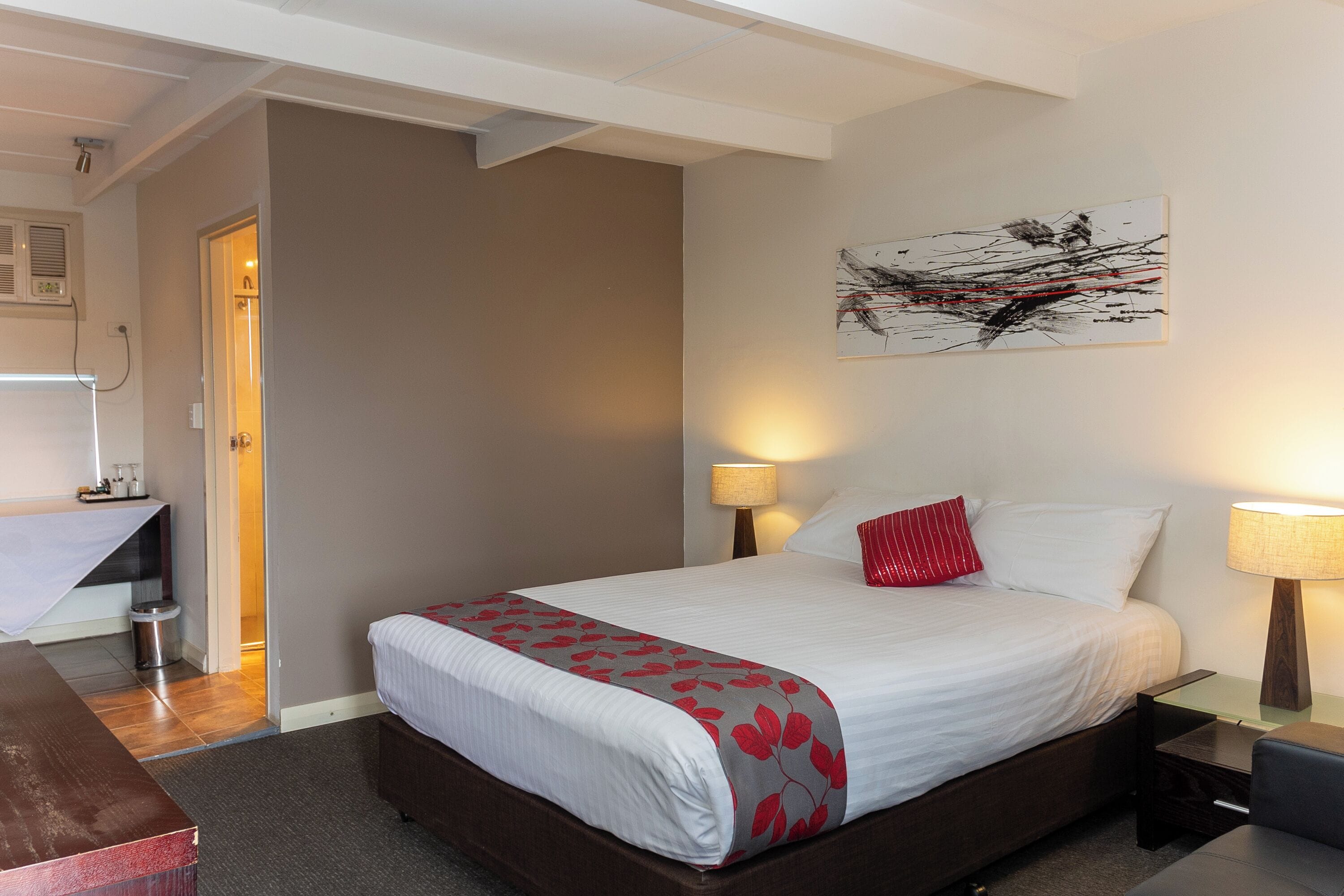 A hotel room with a bed, bedside lamps, a desk, and a wall-mounted abstract painting.